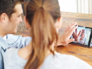 A young couple using a digital tablet for a video call with their family